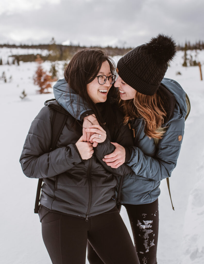 Couple stands together in the snow, laughing during their couples session with Breckenridge proposal photographer