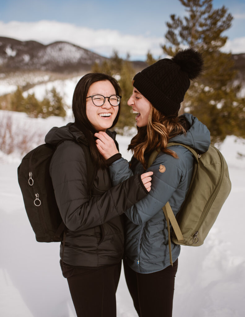 Couple stands together in the snow, laughing during their couples session with Breckenridge proposal photographer