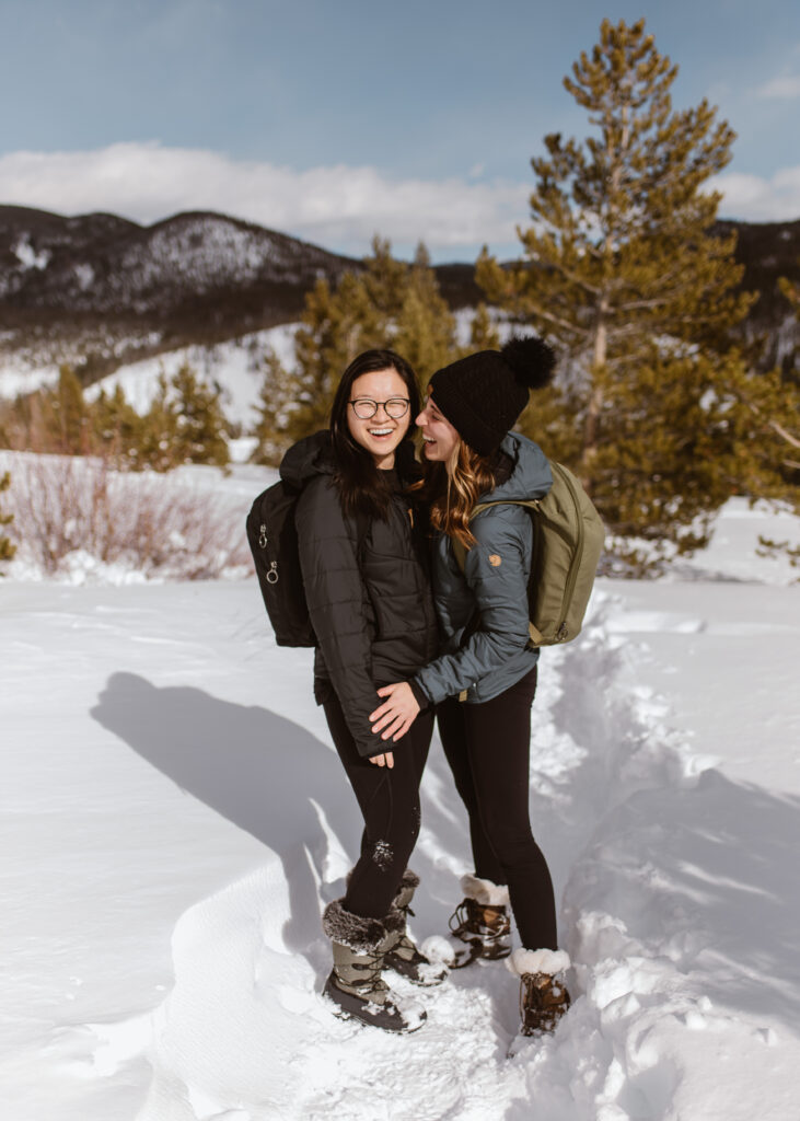 Couple stands together in the snow, laughing during their couples session with Breckenridge proposal photographer