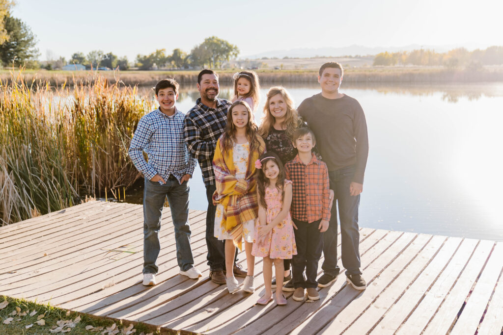 family of 8 portrait by the water on a dock with the sunset in the background