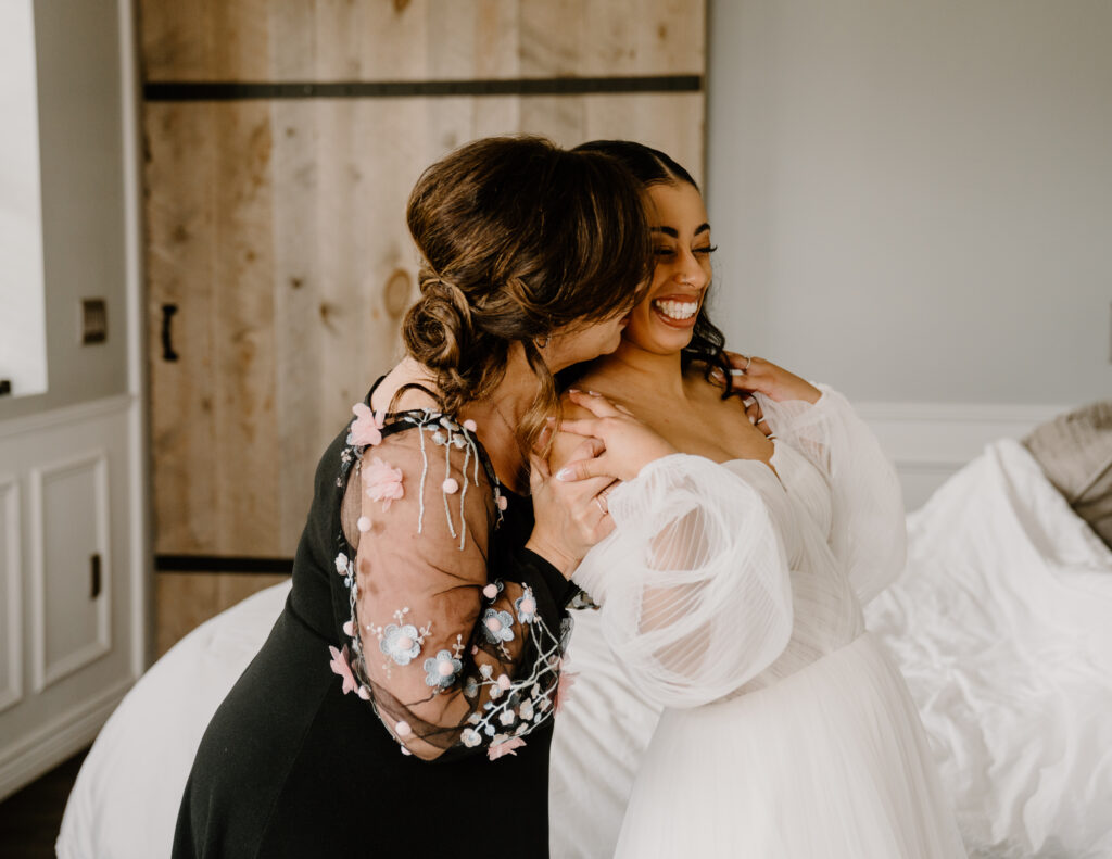 bride putting on earrings while her mom smiles and laughs with her
