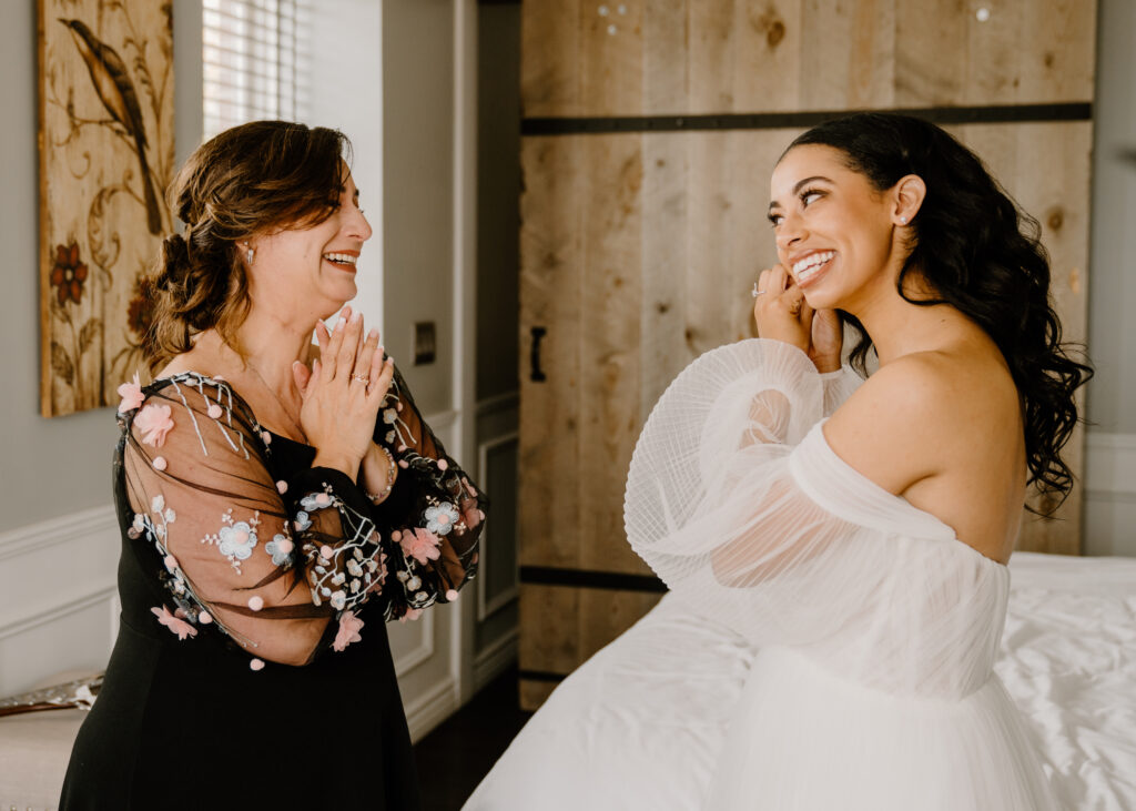 bride putting on earrings while her mom smiles and laughs with her
