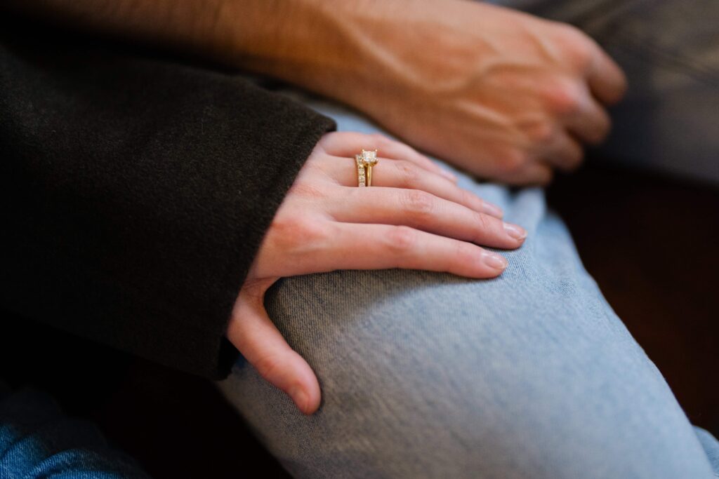 Close-up detail of an engagement ring resting on a partner’s leg.