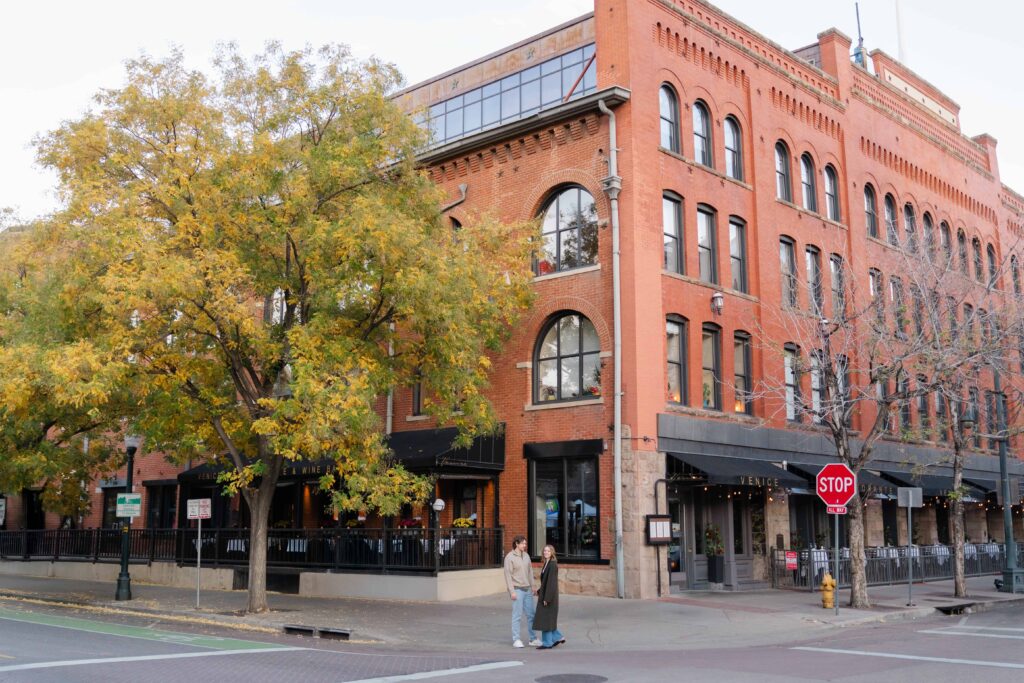Wide shot of couple standing on the corner near historic red-brick buildings and fall trees in downtown Denver