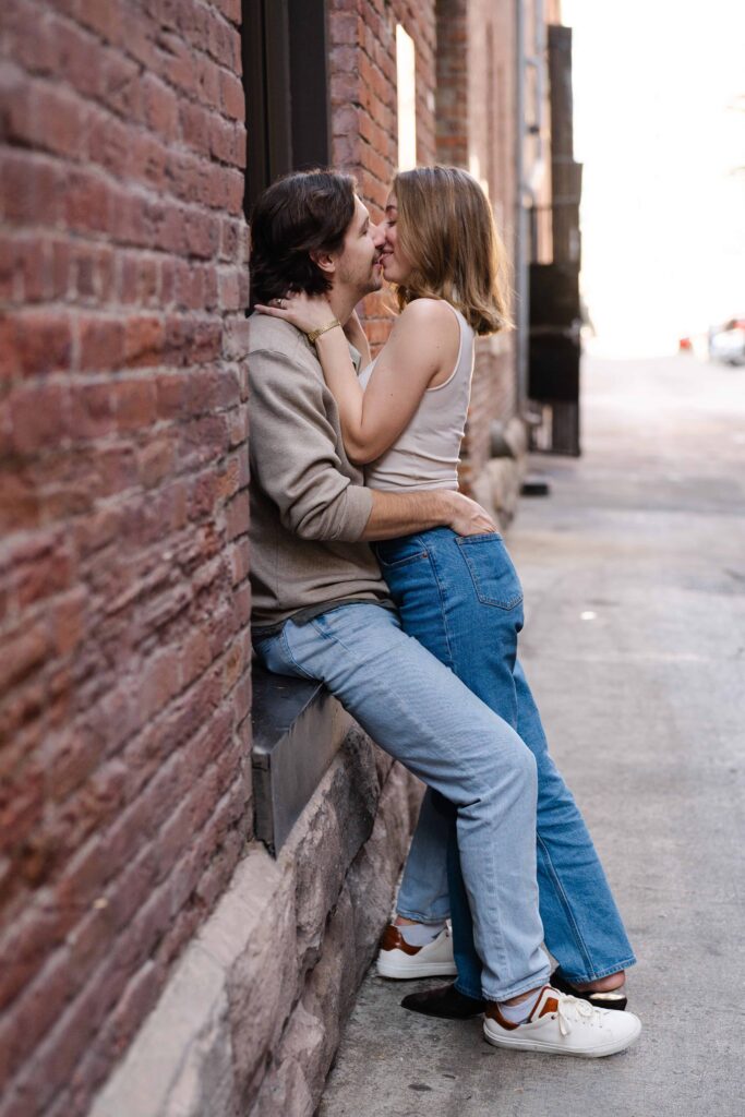 Couple kissing in a brick alley, holding each other closely.
