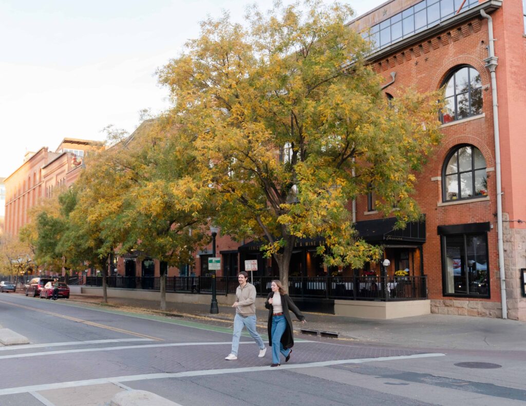 Couple crossing a street surrounded by fall colors and classic Denver brick architecture — Denver engagement photographer