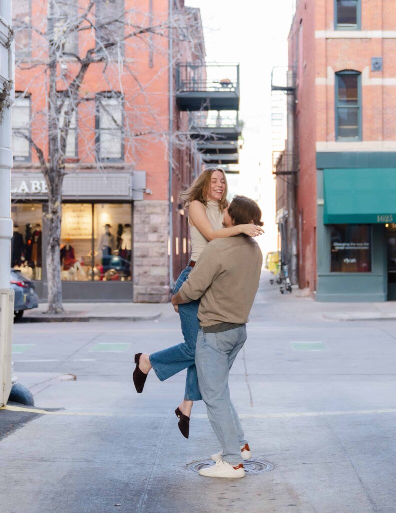 Man lifting his partner off the ground in a downtown Denver alley during a Denver Union Station engagement session.