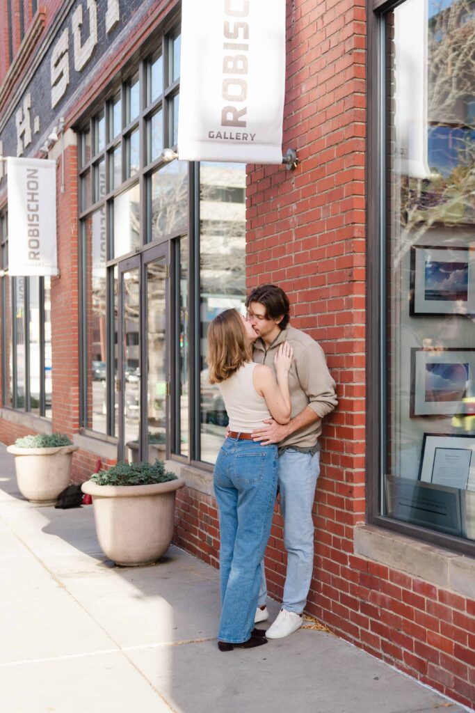 Couple kissing outside the Robischon Gallery, standing against a brick building in downtown Denver.