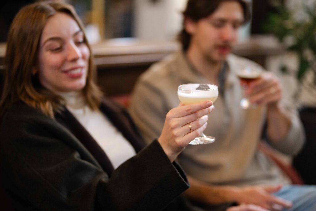 Woman holding a cocktail and smiling while sitting with her partner.
