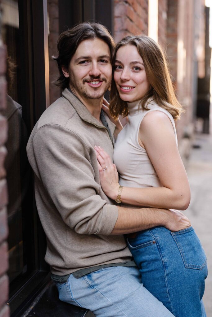 Close-up portrait of the couple standing against a brick wall, smiling at the camera.