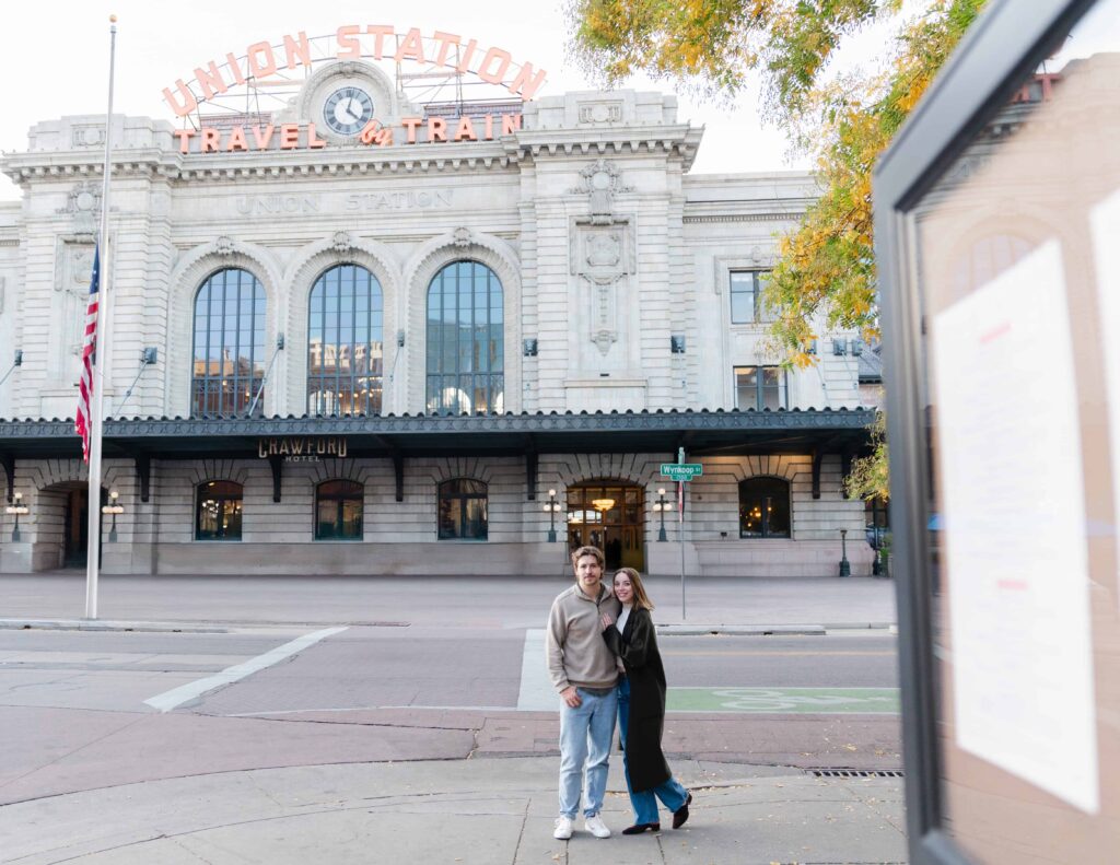 Engaged couple smiling outside Denver Union Station with the historic façade behind them