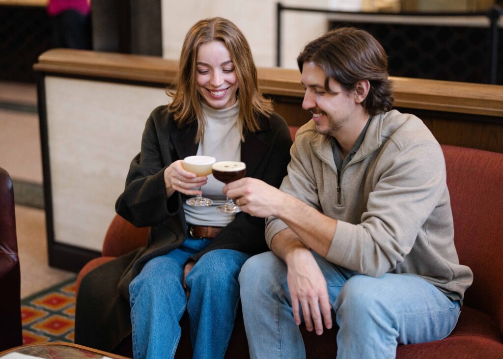Couple sitting on a red couch, clinking cocktail glasses and smiling.