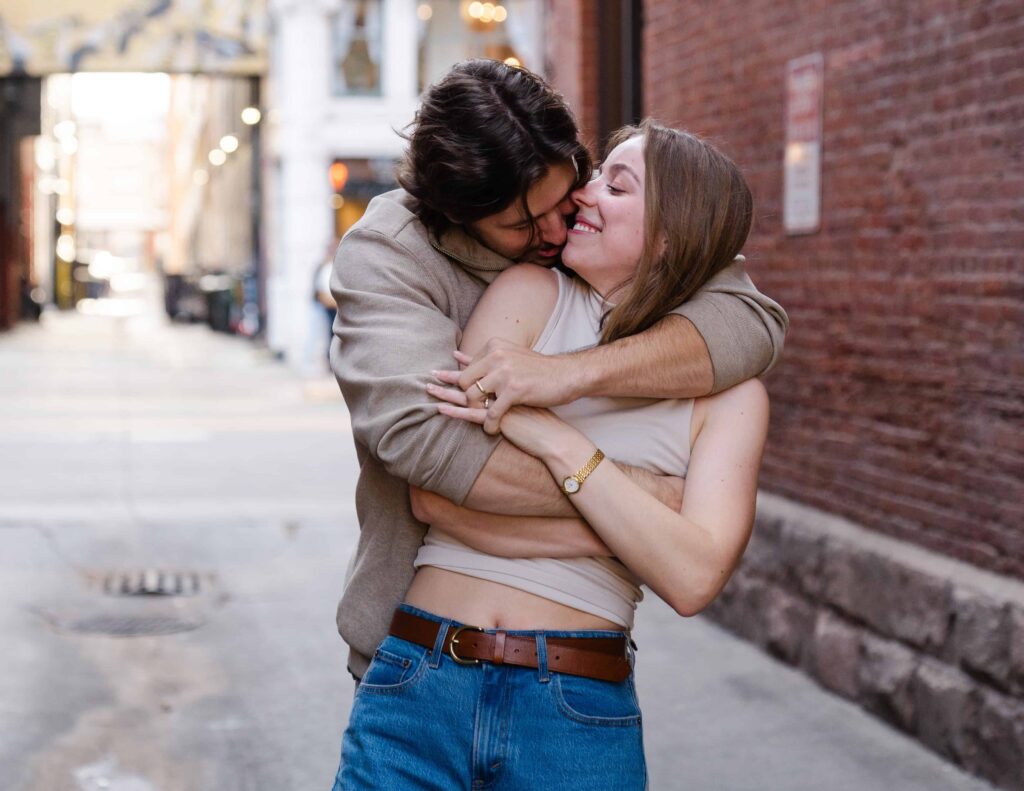 Playful moment as he hugs her from behind in a downtown Denver alley during their engagement session.