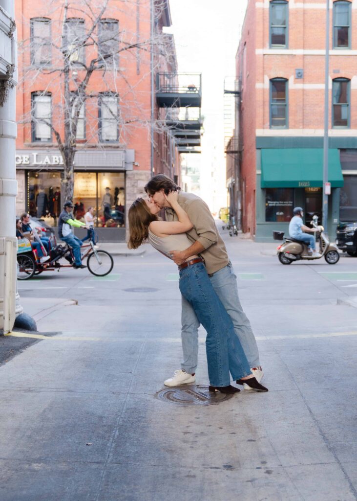 Couple kissing in the middle of a downtown street while a pedicab and scooter pass behind them.