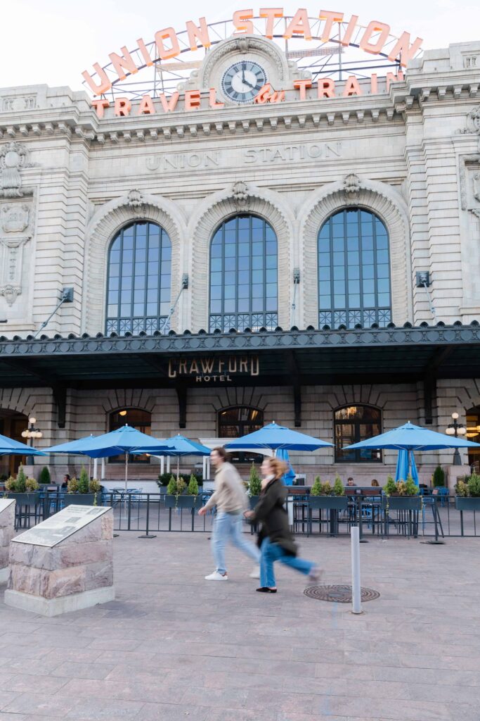 Couple walking hand in hand in front of Denver Union Station, motion blur capturing an authentic candid moment — Denver engagement photographer