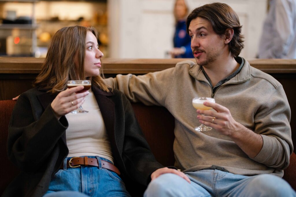 Couple talking on a couch at Union Station, each holding a cocktail.