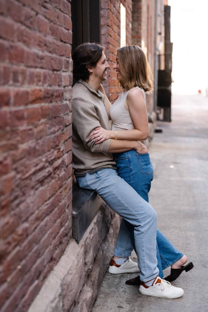 Couple standing in a narrow brick alley, holding each other and smiling during a Denver engagement photographer session.